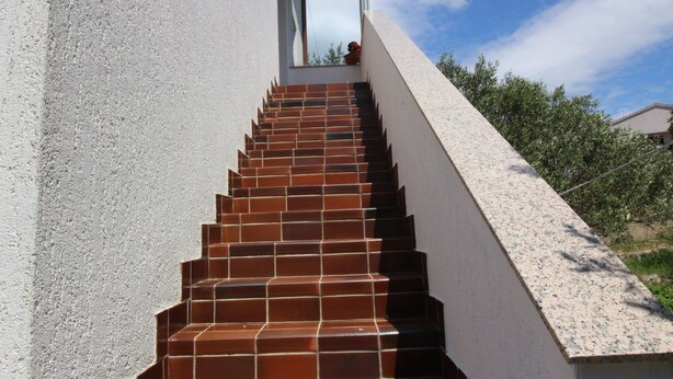 Un escalier aux marches marron menant à une porte, le tout entouré d’un mur blanc et d’un ciel dégagé.