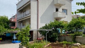 Un immeuble à plusieurs étages doté de balcons, un espace jardin avec des plantes et un petit étang, ainsi qu’un chemin pavé.