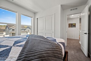Une chambre avec un grand lit, des murs blancs et une vue sur les maisons voisines.
