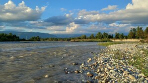 A riverbank with a rocky shoreline, trees, and mountains in the background. - Stunning private villa with WIFI, A/C, hot tub, private pool, sauna, TV and pets allowed (Montebelluna)