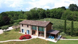 A two-story stone house with a tiled roof, a covered porch with blue chairs, and a well-maintained garden with red flowers. - Stunning private villa with WIFI, A/C, hot tub, private pool, sauna, TV and pets allowed (Montebelluna)