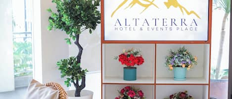 Segnaletica per l'Hotel & Location eventi Altaterra, con logo, circondata da piante in vaso e una sedia in vimini.