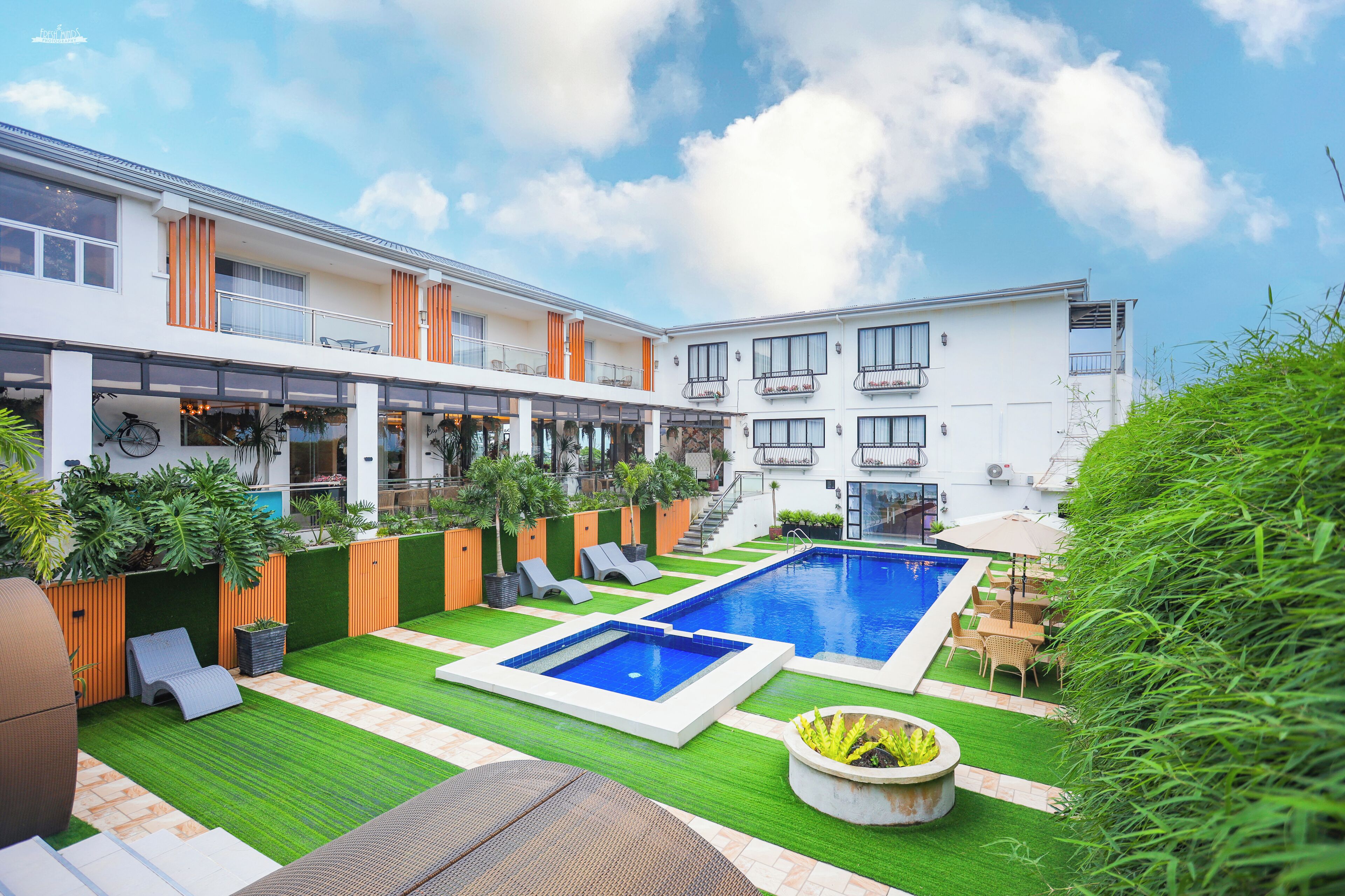 Un hôtel moderne doté d’une cour intérieure avec piscine, d’une pelouse verdoyante et d’un espace extérieur aménagé pour se détendre.