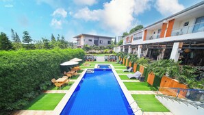 A swimming pool with a clear blue water, surrounded by green grass and plants, and a building with balconies in the background. - Alta Terra Hotel Tagaytay (Tagaytay)