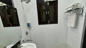 Ένα μπάνιο με έναν λευκό νιπτήρα, έναν καθρέφτη, μια κρεμάστρα για πετσέτες, έναν ανεμιστήρα και ένα ντους.