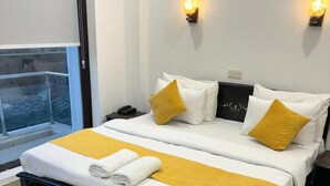 Ένα διπλό κρεβάτι με λευκά και κίτρινα σεντόνια, δύο φωτιστικά κομοδίνου, ένα κομοδίνο και ένα παράθυρο με θέα.