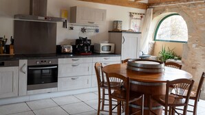 Une cuisine avec des poutres en bois, un four en acier inoxydable, une table ronde en bois et un mur en pierre avec une fenêtre.