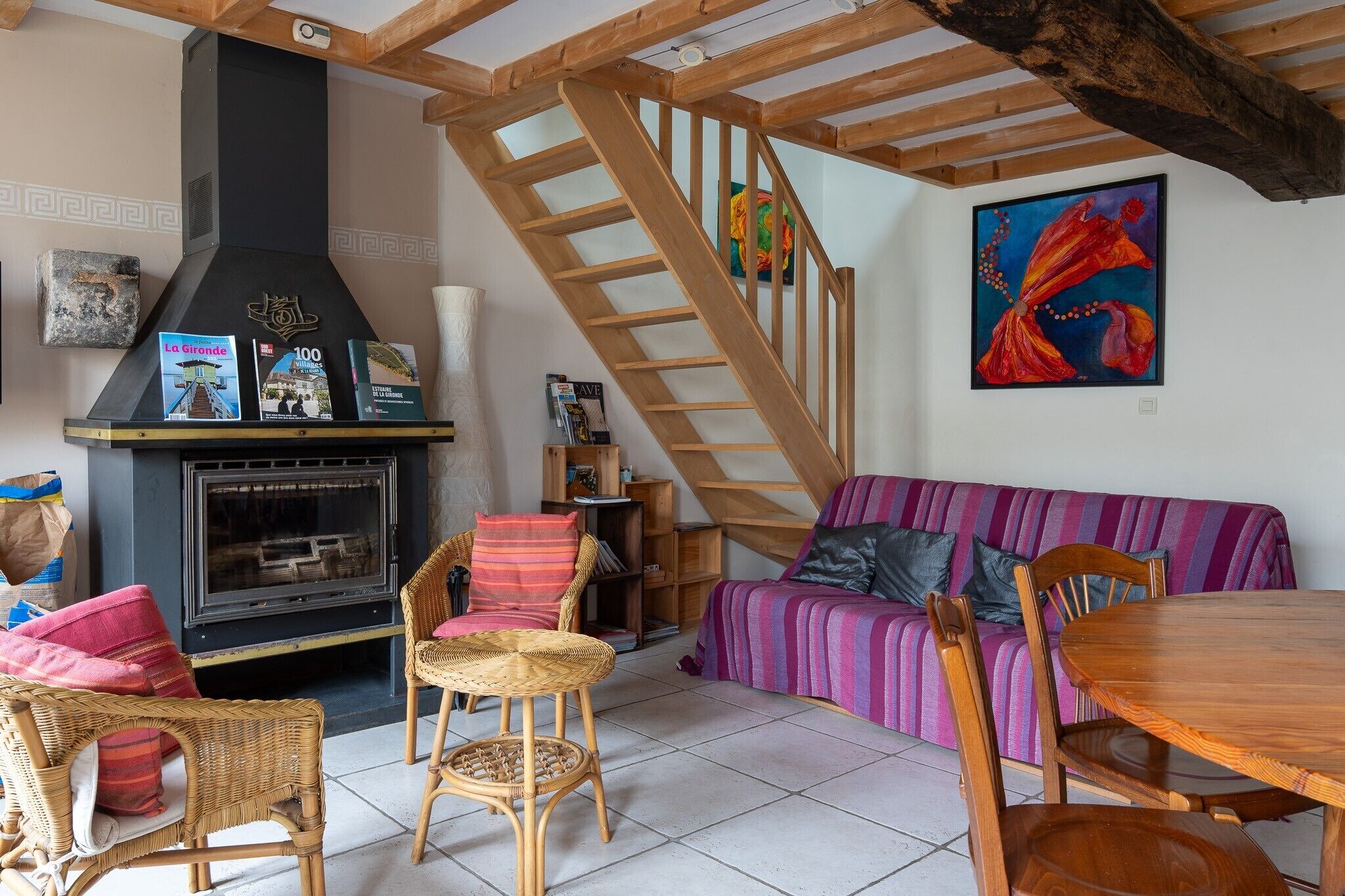 Un salon chaleureux avec une cheminée, un escalier en bois et un tableau aux couleurs vives.
