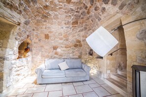 Une pièce aux murs de pierre, avec un canapé de couleur claire et un luminaire suspendu.