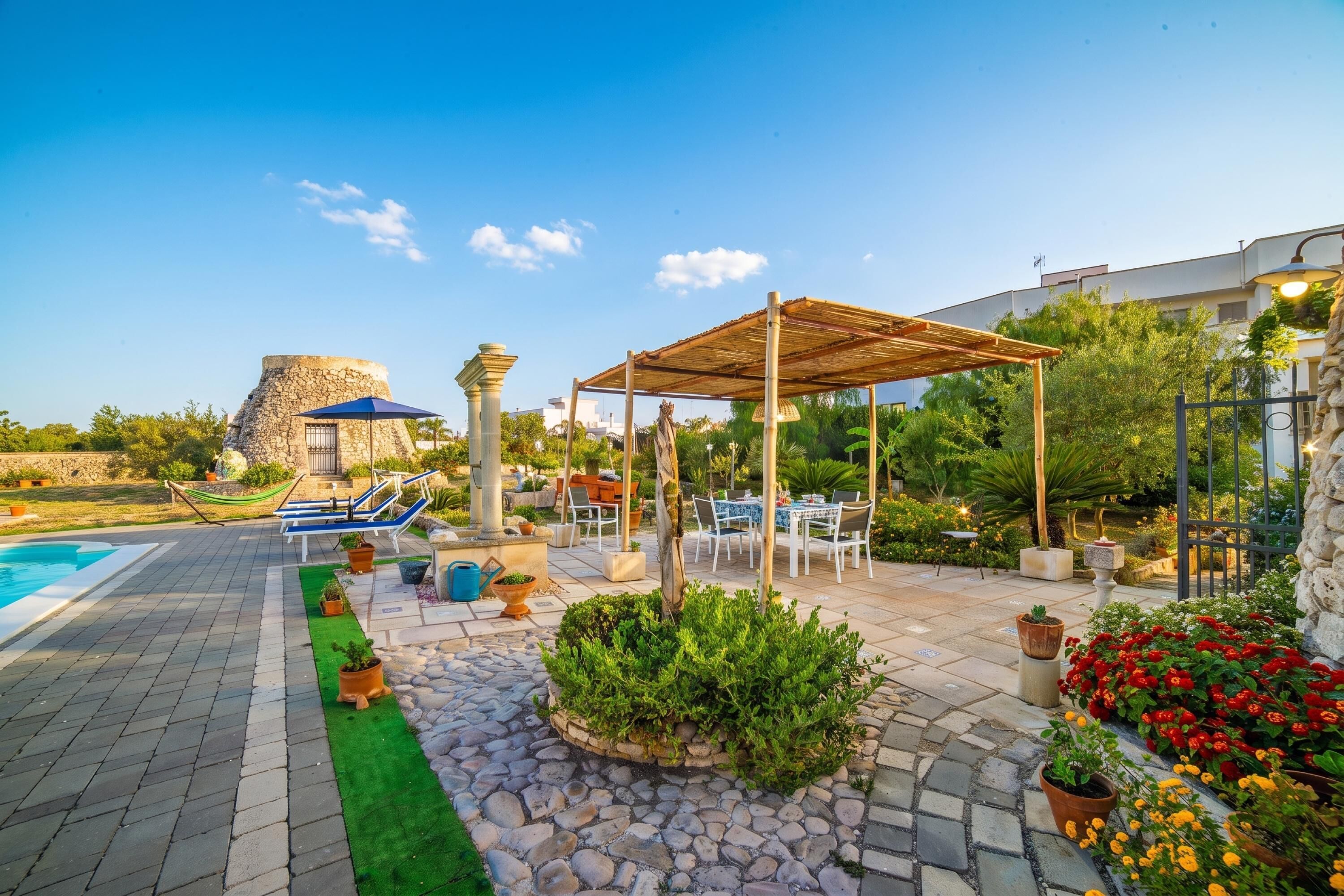 A pool area with lounge chairs, a pergola, and a stone wall.