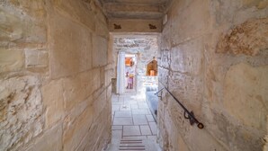 A narrow stone corridor with a tiled floor leading to a room with a stone wall and a window. - Tenuta Apollonio Pool & Relax (Carpignano Salentino)
