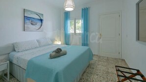A bedroom with a bed, a painting, a hanging light fixture, and a window with curtains.