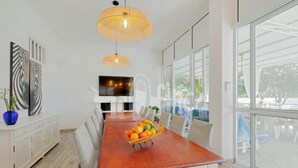 A modern dining area with a wooden table, white chairs, and a fruit basket.