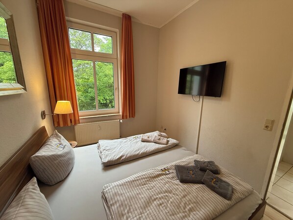 Una habitación de hotel con cama, televisión montada en la pared, ventana con cortinas y lámpara.