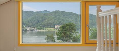 Una habitación con un amplio ventanal con vistas a un lago, un edificio al otro lado del agua y una colina boscosa.