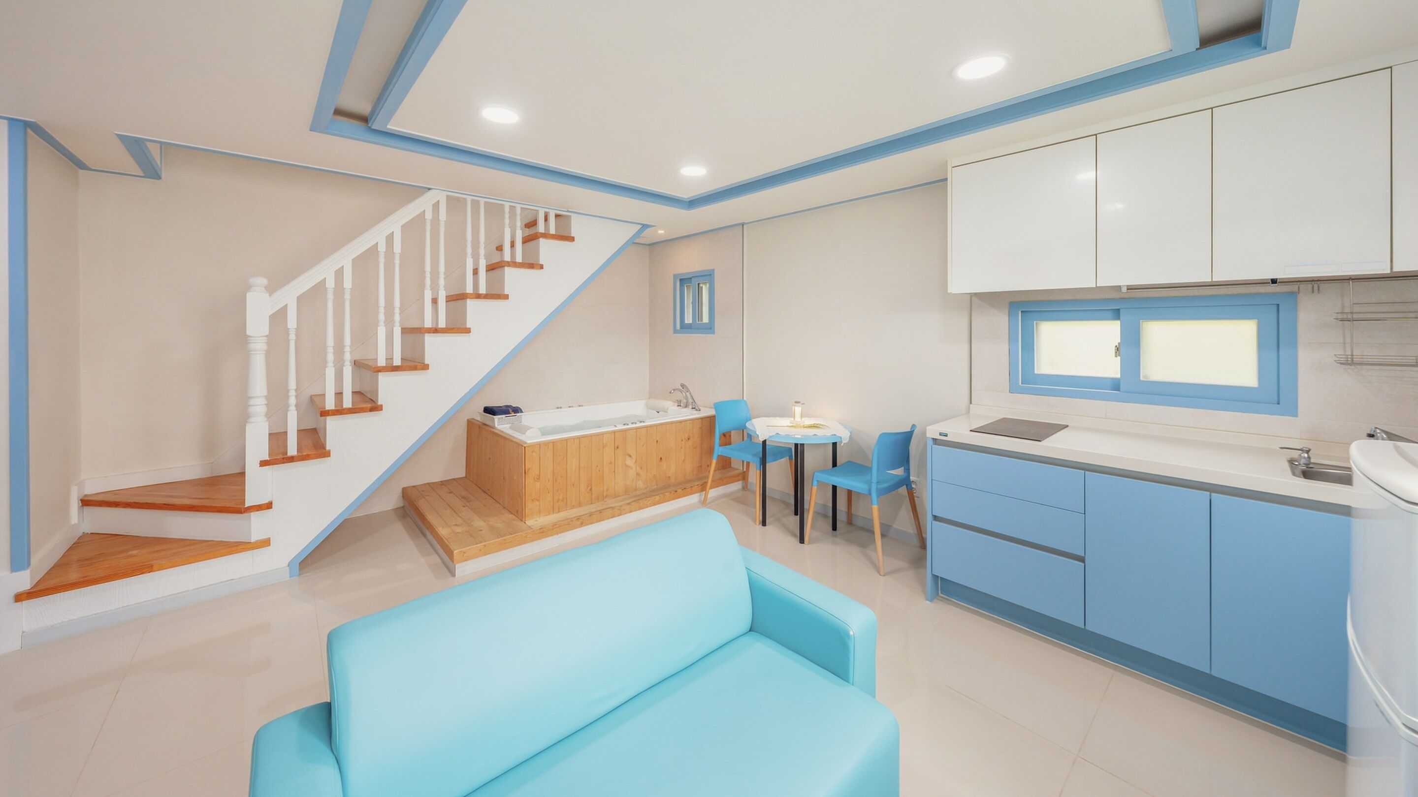 A modern kitchen with blue cabinets, a wooden staircase, and a blue sofa.