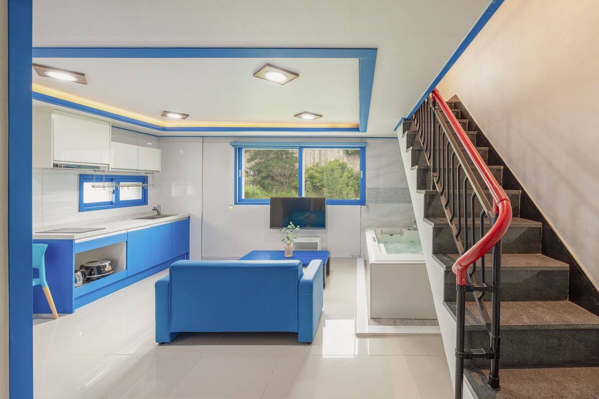 Eine moderne Küche mit blauen Schränken, einem Essbereich und einer Treppe mit roten Geländern.
