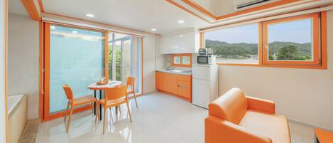 Eine moderne Küche mit Aussicht, ein Essbereich mit orangefarbenen Stühlen und eine Sitzecke mit einer Couch.