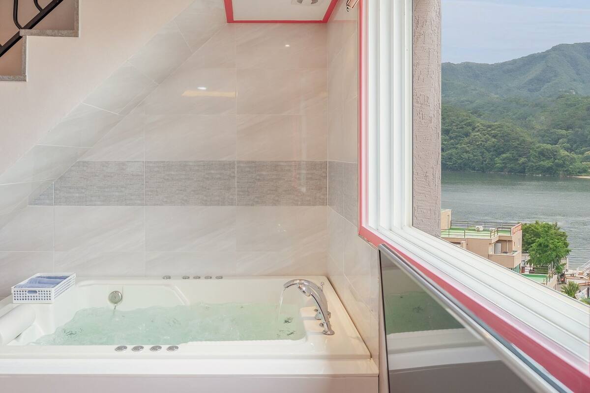 Ein Badezimmer mit einer Badewanne, einem Fenster mit Blick auf einen See und Berge sowie einer Treppe.