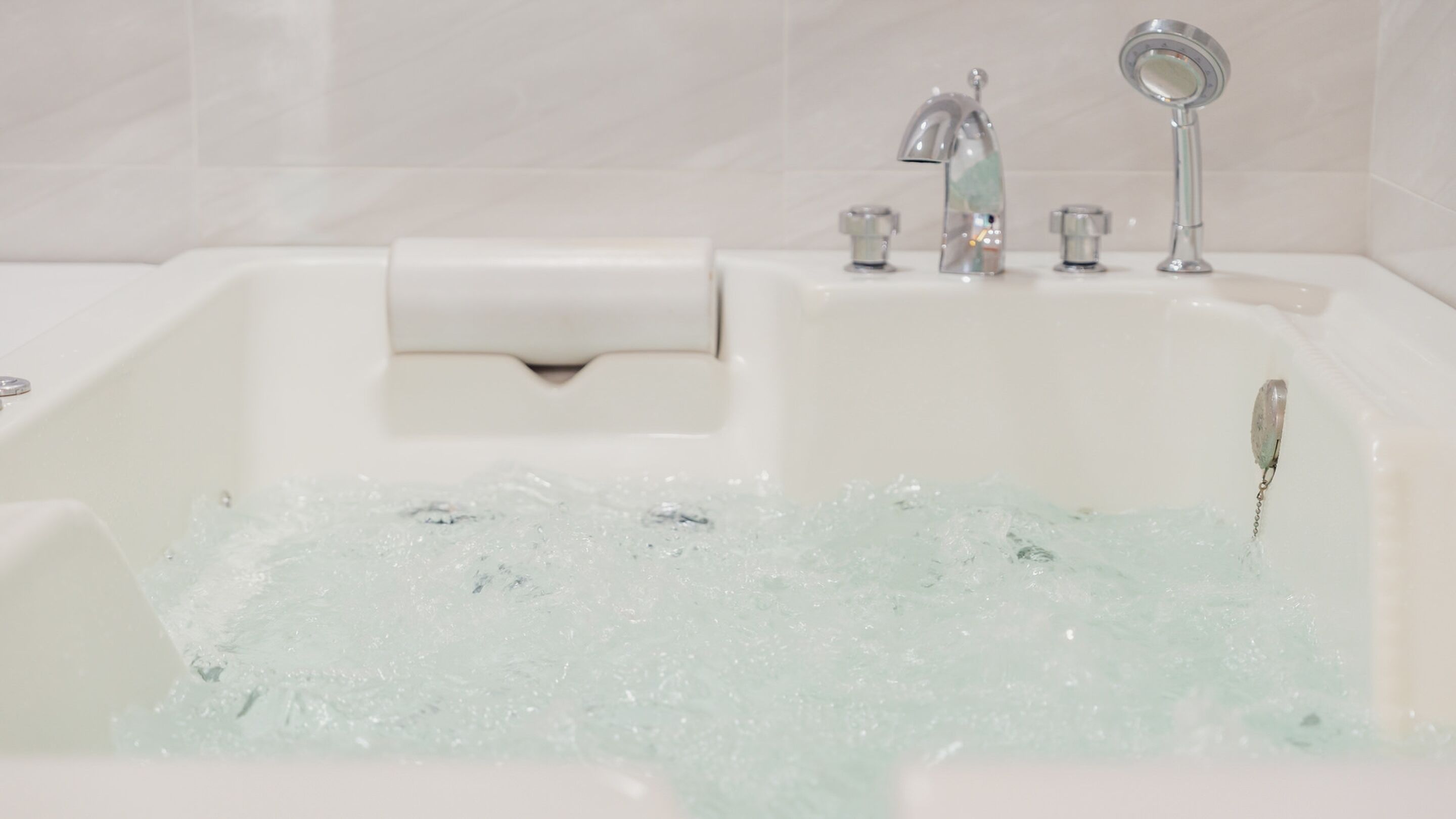 A bathtub with running water, a soap dispenser, and a handheld showerhead.