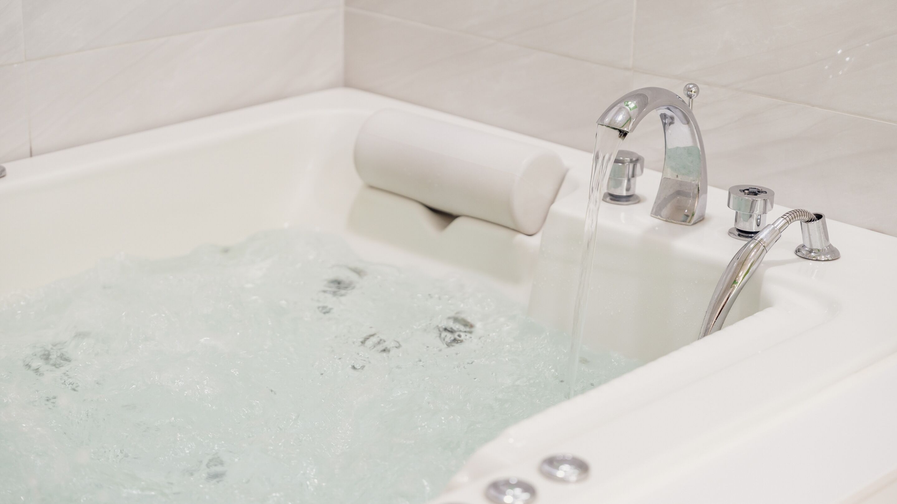 A white bathtub with running water and a rolled-up bath mat.