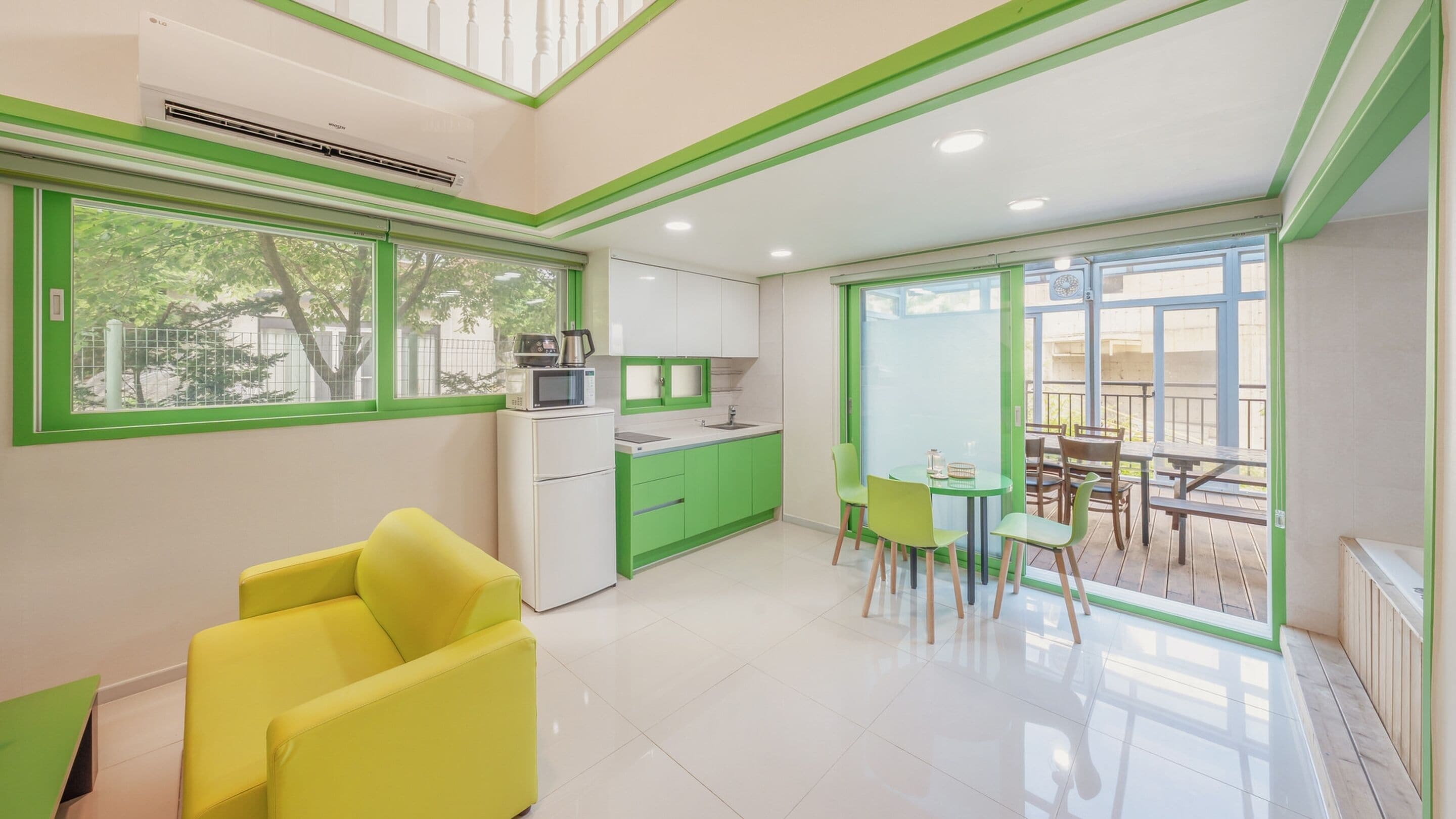 A modern kitchen with green accents, a dining area with a table and chairs, and a bright yellow armchair.