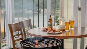 Uma mesa redonda com uma churrasqueira, uma garrafa de cerveja e espetos de carne.