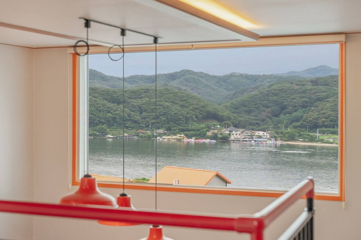 Ein Zimmer mit großem Fenster mit Blick auf einen See und Berge.