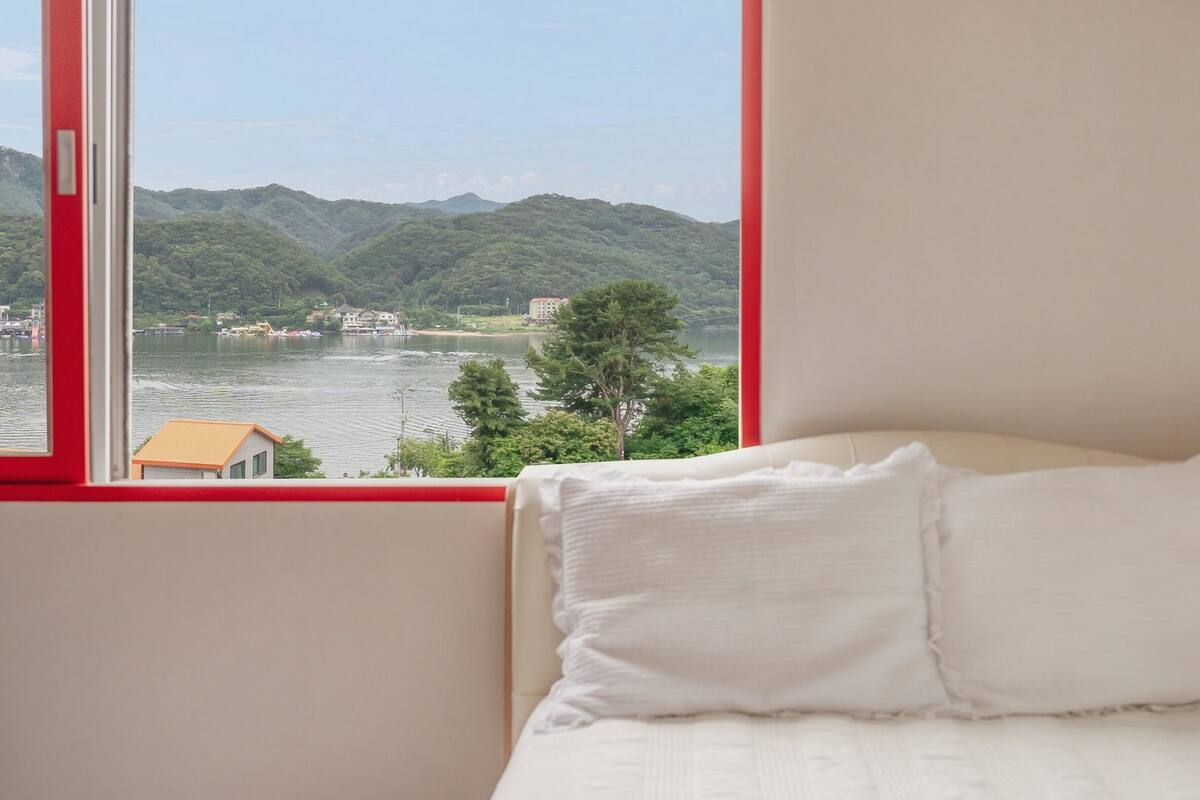 Ein Schlafzimmer mit einem Bett, einem Fenster und Blick auf einen See und Berge.