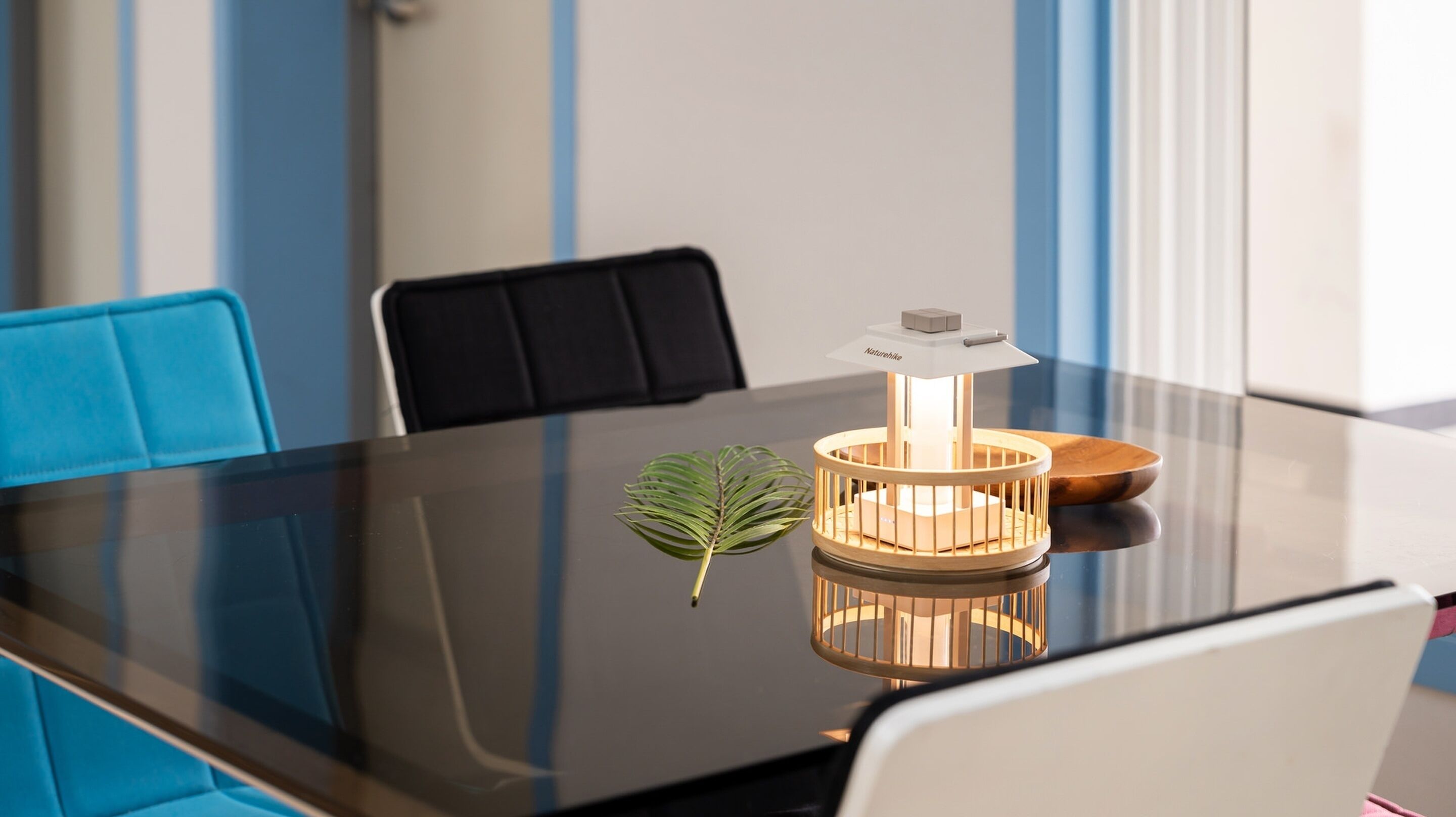 Una mesa de conferencias con una lámpara moderna, una planta en maceta y una maqueta de una casa encima.