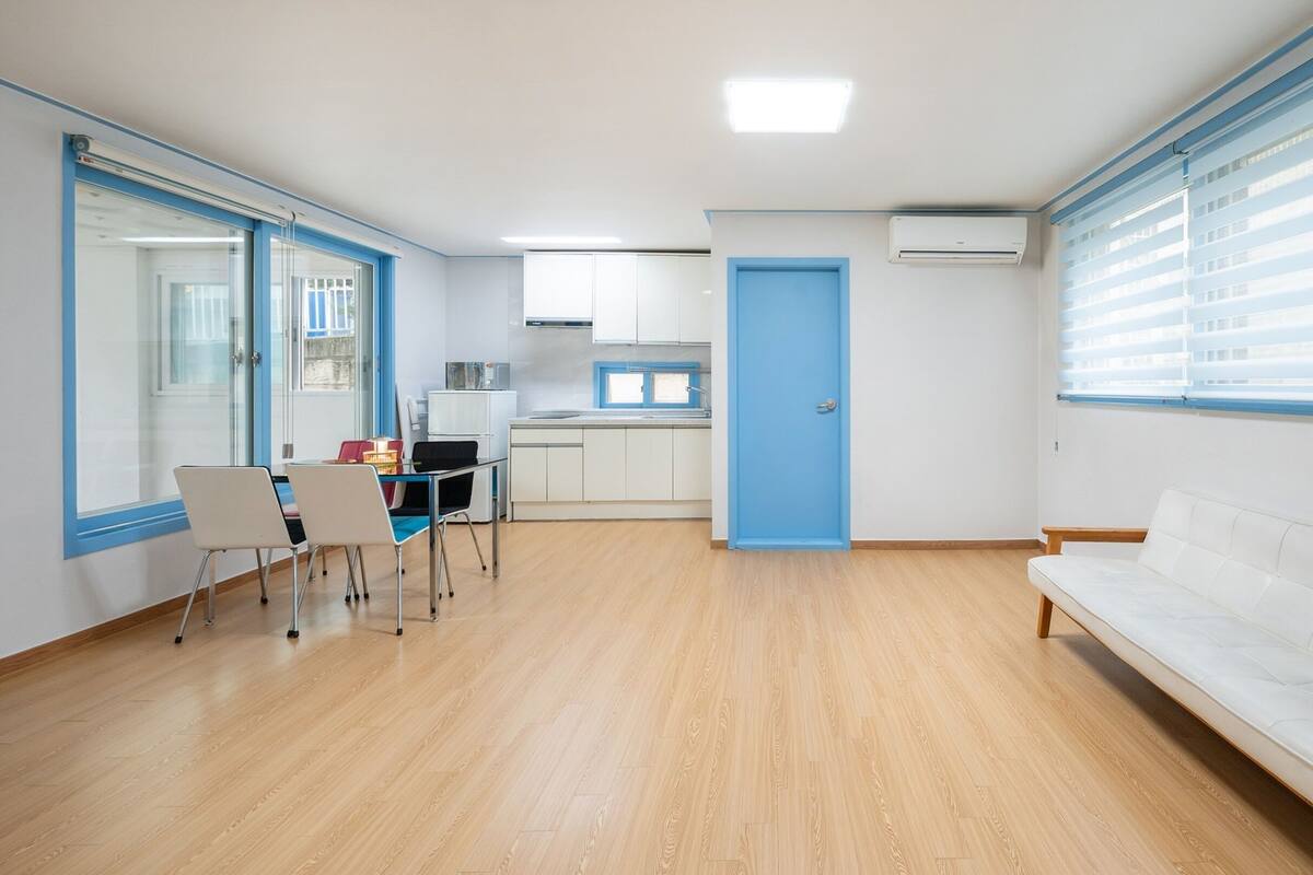 Ein modernes Wohnzimmer mit einem weißen Sofa, einer Essecke mit Stühlen und einem Tisch sowie einer Küche im Hintergrund.