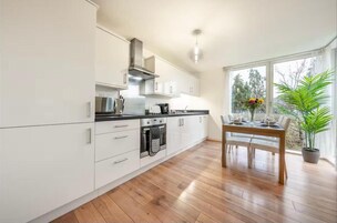 Una cocina moderna con armarios blancos, una encimera negra y una mesa de comedor de madera con sillas.
