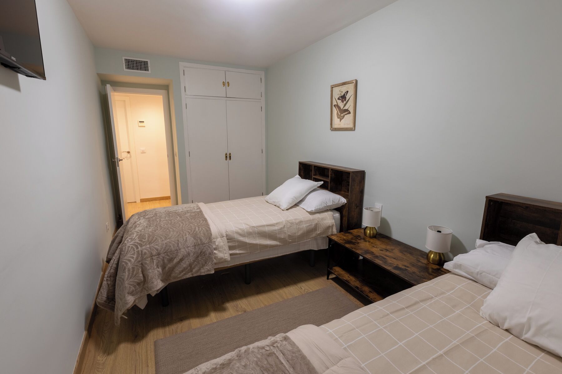Een knus slaapkamer met twee eenpersoonsbedden, een houten nachtkastje, een nachttafel en een garderobe.