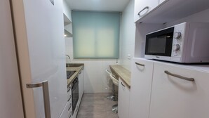 Een smalle keuken met witte kastjes, een magnetron en een raam met uitzicht.