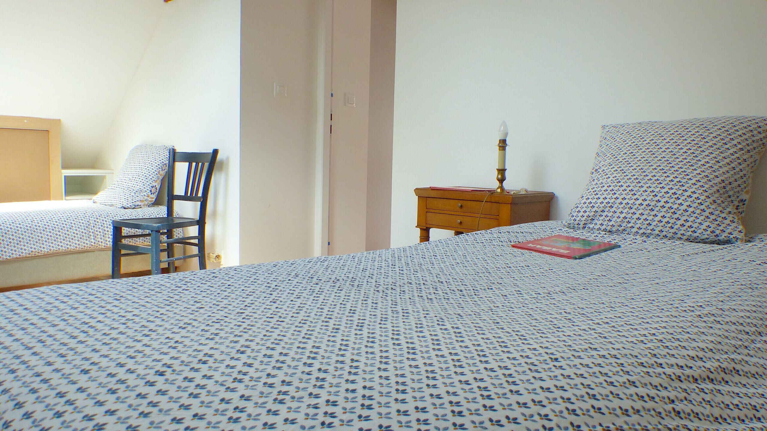 A bedroom with two beds, a chair, a nightstand, and a lamp.