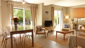 A well-lit living room with a dining area, a television, and a view of greenery outside.