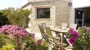 An outdoor dining area with a stone wall, a window, and a table set for two.