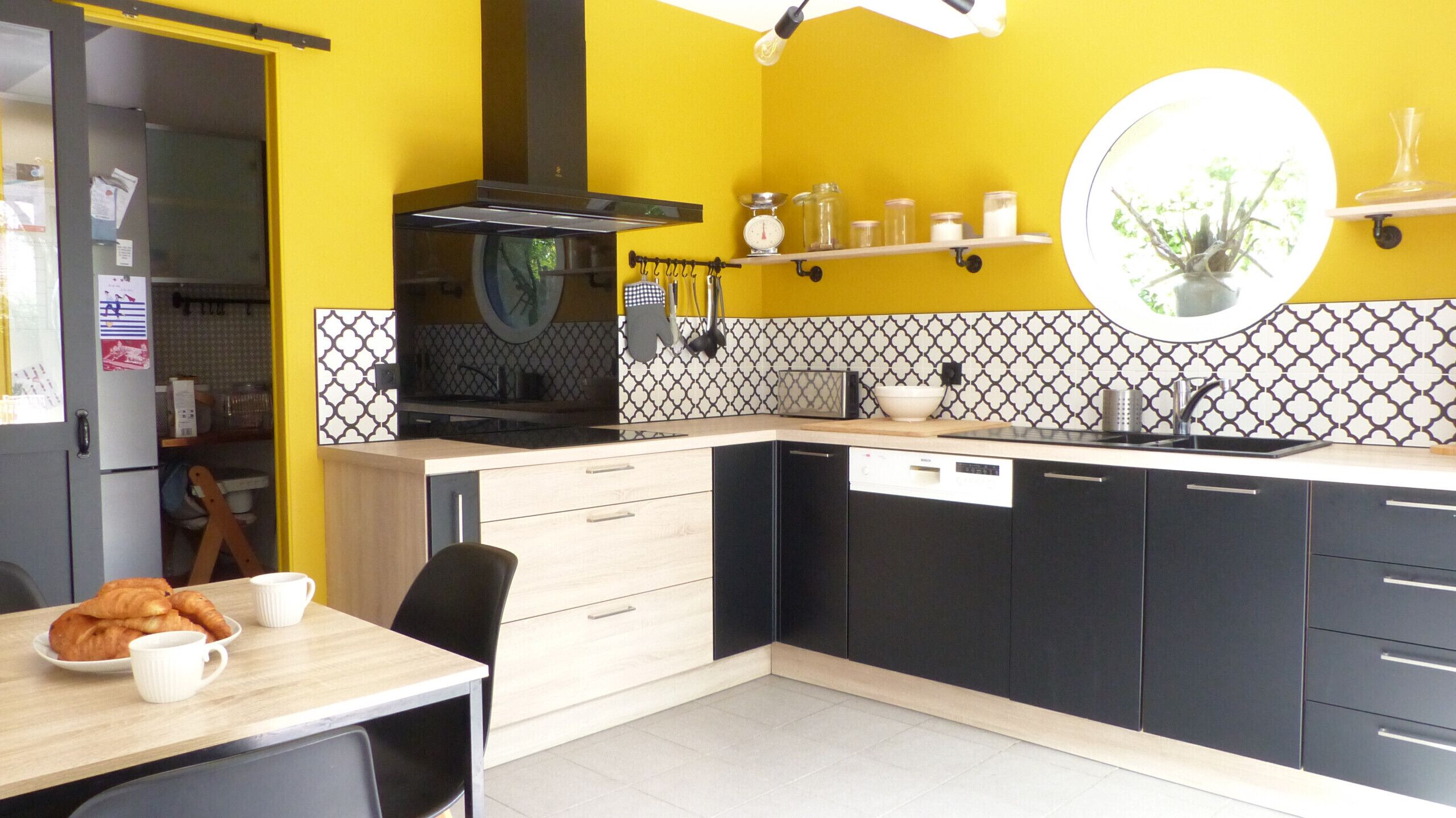 A kitchen with a yellow wall, black cabinets, and a white countertop. There is a sink, a stove, and a dining area with a table and chairs.