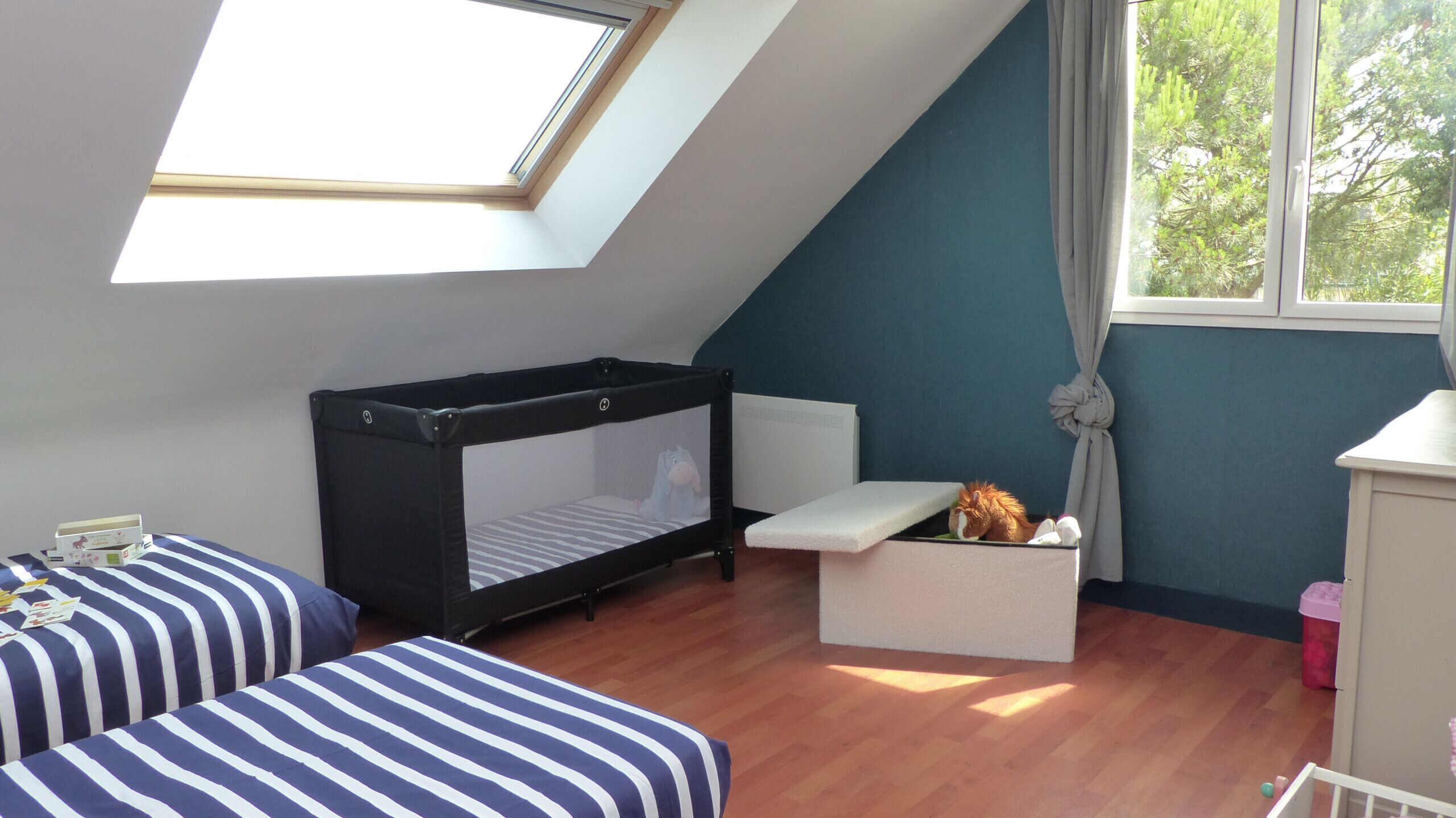 Une chambre avec un lit superposé, un petit bureau, une fenêtre avec des rideaux et une vue sur les arbres à l’extérieur.