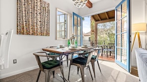 A dining area with a table set for four, chairs, a chandelier, and a view through open doors to an outdoor patio.