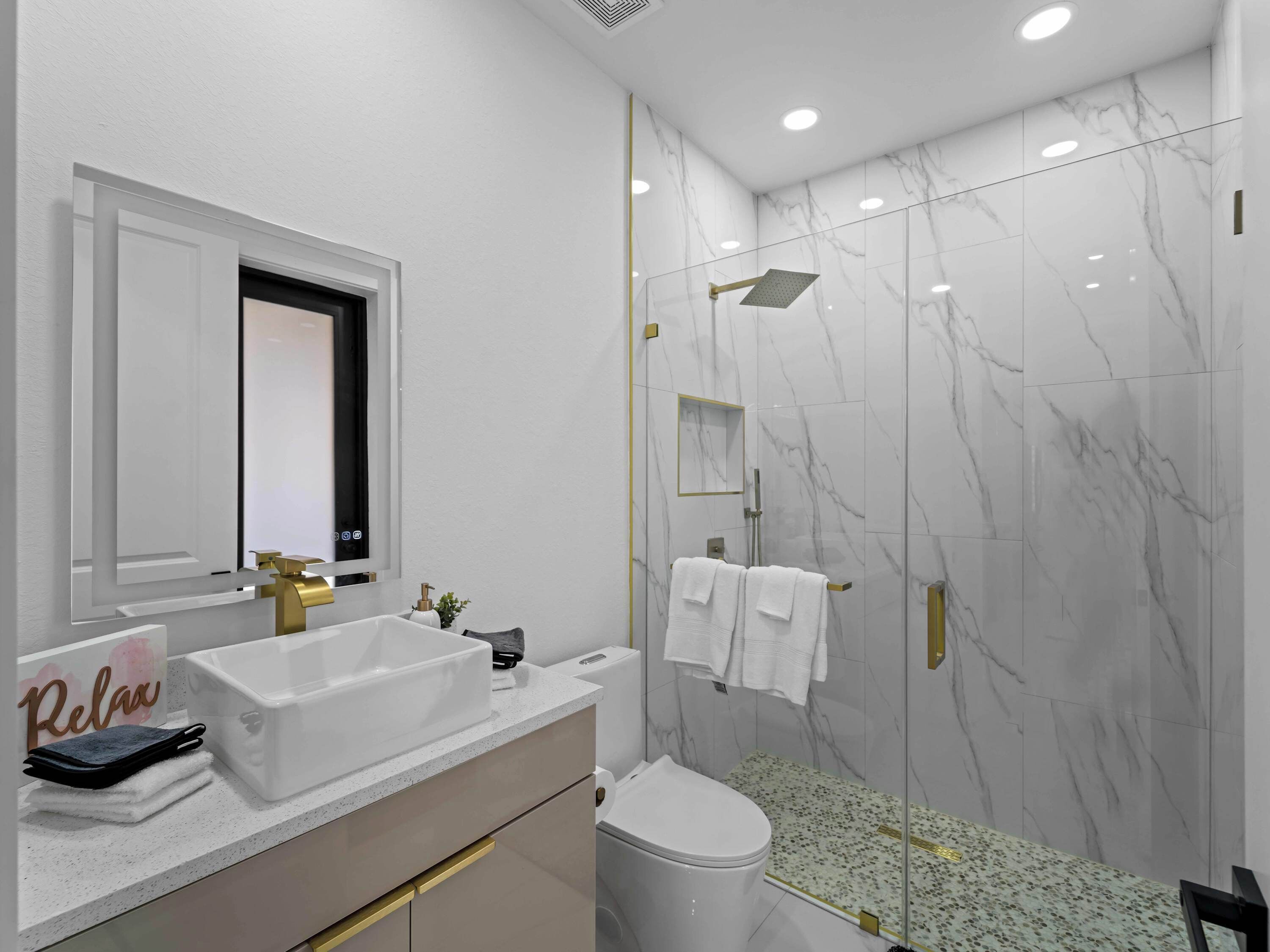 Un bagno moderno con lavandino bianco, accessori dorati, cabina doccia in vetro e pareti in marmo.