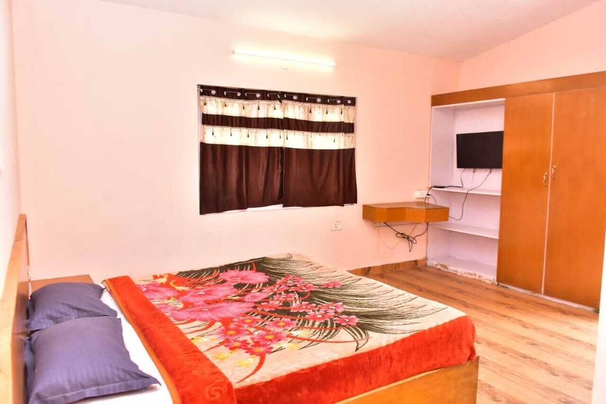 A bedroom with a bed, a TV, a wardrobe, and a window with curtains.