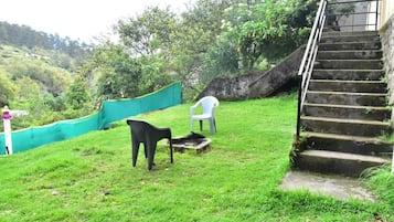Une zone herbeuse avec un escalier menant vers le haut, une chaise en plastique blanche et une chaise en plastique noire.