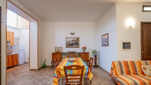 Zona pranzo con tavolo, sedie, divano e cucina sullo sfondo.