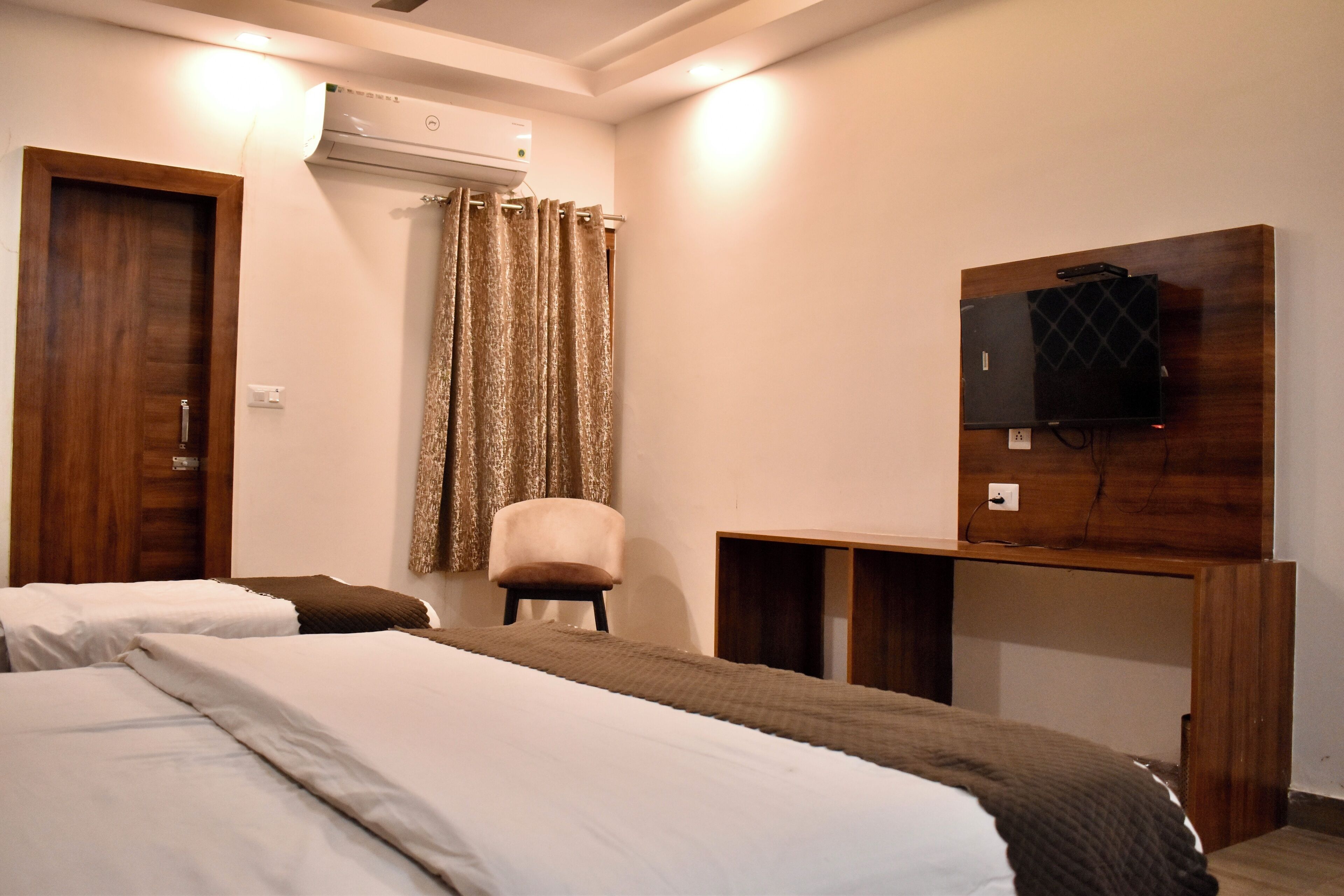 A hotel room with two beds, a chair, a TV, and a desk.