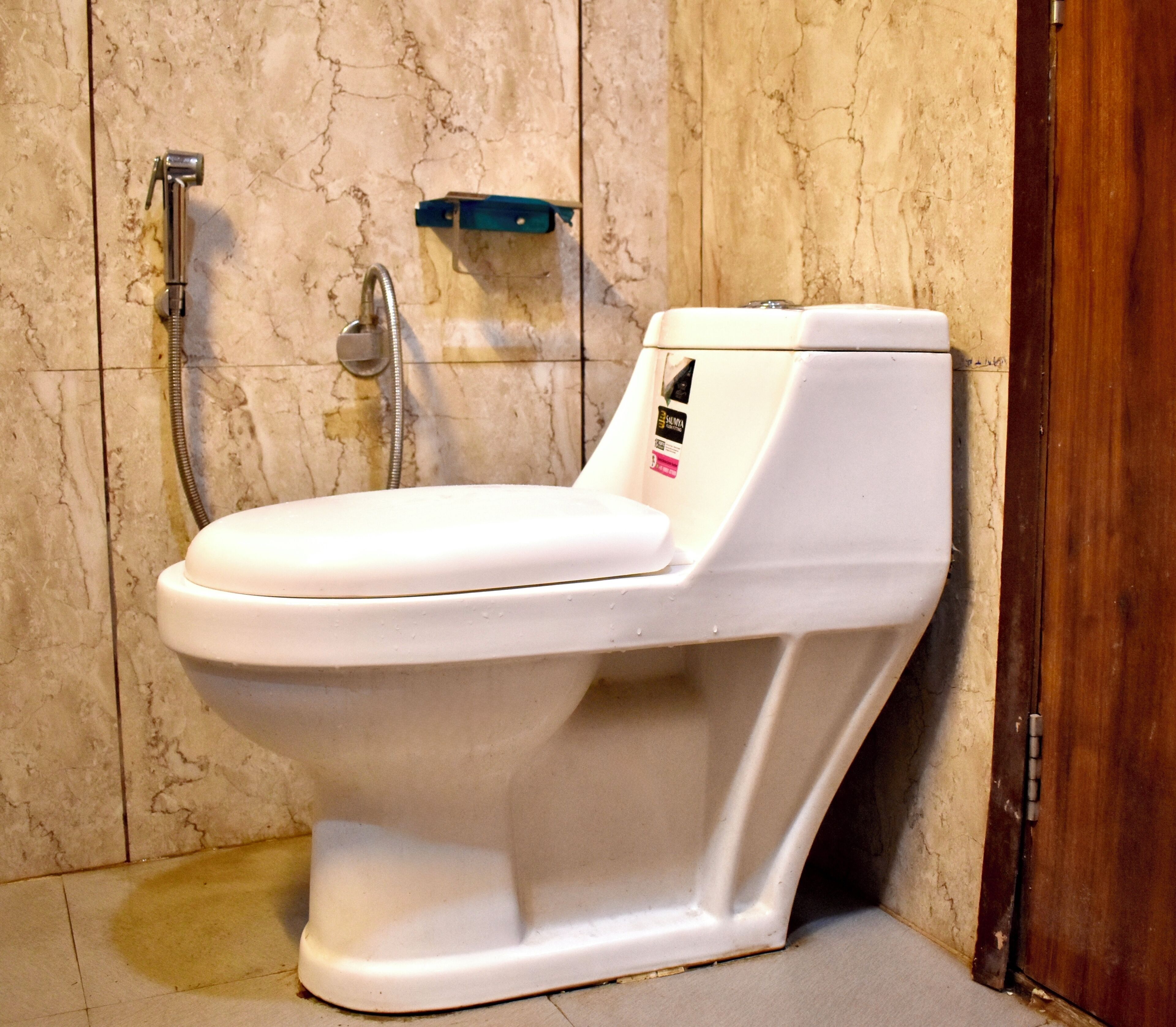 Un inodoro blanco en un baño con pared de mármol y puerta de madera.
