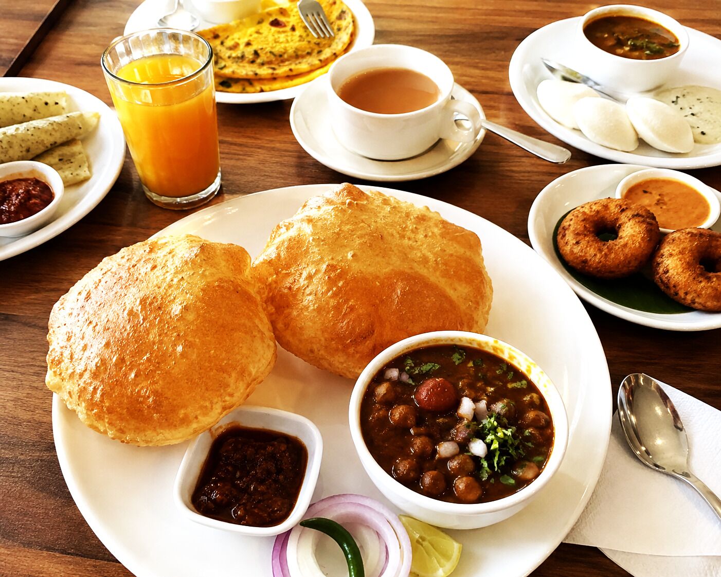 A breakfast setting with various dishes including flatbreads, a bowl of soup, and a glass of orange juice.