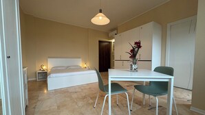Un dormitorio con cama, lámparas de noche, mesitas de noche, una mesa de comedor con sillas y un jarrón con flores.