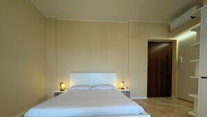 Un dormitorio con una cama grande, dos mesitas de noche con lámparas, un armario y una puerta.
