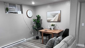 A modern living room with a grey sofa, a wooden dining table, a potted plant, a wall clock, and a framed picture of a pier. - Duluth Delight #1 Sum (Sioux Falls)